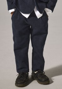 Marineblaue Kariersakko-Hose aus strukturiertem Stoff, kombiniert mit schwarzen Lederschuhen im Mokassin-Design und Gummisohlen.