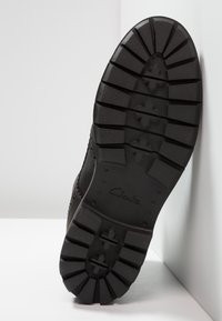 Suola nera di scarpa con scanalature profonde, realizzata in gomma. Presenta una superficie texturizzata e un tacco a blocco; logo "Clarks" inciso vicino al tacco.