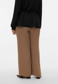 Zwiewna czarna bluzka ze ściągaczem w talii, zestawiona z luźnymi jasnobrązowymi spodniami i ciemnobrązowymi butami. Gładka faktura, minimalistyczny design.