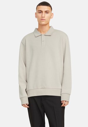 Suéter gris claro con cuello tipo polo, tres botones y mangas largas. Presenta un dobladillo acanalado y una tela texturizada. Llevado sobre pantalones negros.