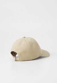 Casquette de baseball beige avec une visière courbée, fabriquée en coton. L'arrière possède une sangle ajustable et des trous de ventilation sur le sommet.