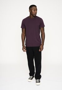Lilla bomulds t-shirt med rund hals, parret med sorte bukser og sorte sneakers med hvide detaljer. Modellen står i profil.