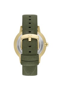 Reloj de oro con una correa de tela verde. La correa tiene una textura suave y múltiples agujeros para ajustar. Hebilla de clip con logo grabado.