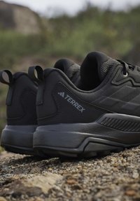 Een paar zwarte Adidas Terrex wandelschoenen op rotsachtige ondergrond met gestructureerde zolen en ademende mesh bovenwerken.