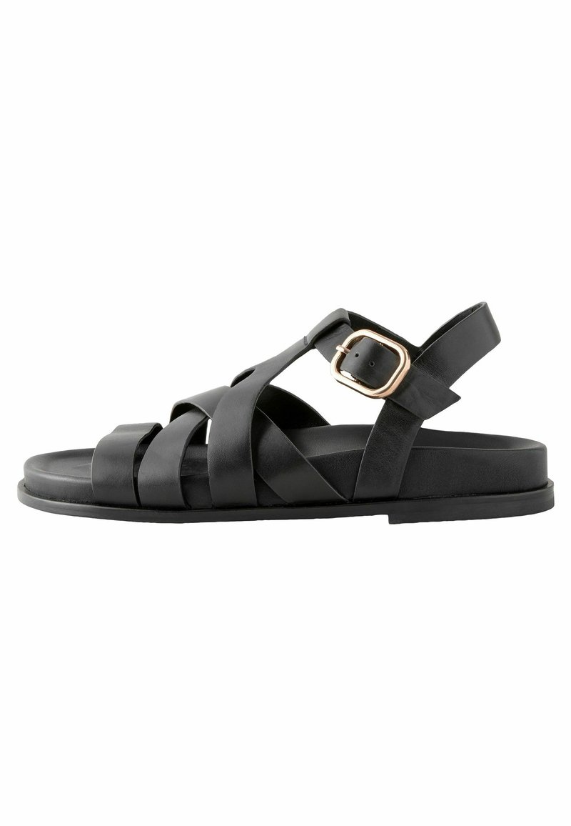 Sandale plate en cuir noir avec plusieurs brides et une fermeture à boucle dorée sur fond blanc.