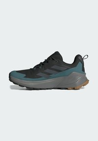 Trailrunning-Schuh mit schwarzem und türkisfarbenem Obermaterial, strukturierten Überzügen, grauer Zwischensohle und rutschfester Gummisohle für Grip und Unterstützung.