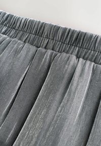 Graues, plissiertes Gewebe mit glänzender Textur. Elastischer Bund sichtbar an der Oberseite. Glatte Oberfläche mit subtiler Glanz und feinen Nähdetails.