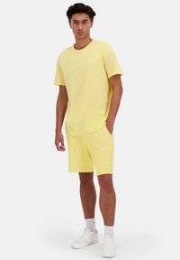 Camiseta de algodón amarilla con cuello redondo, combinada con pantalones cortos amarillos a juego. Los zapatos son blancos con detalles sutiles.