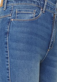 Jeans de ganga azul com uma vista de perto, apresentando uma textura suave, desbotamento subtil e costura contrastante ao longo das costuras e bolsos.