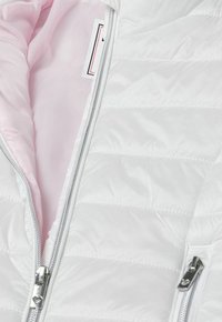 Giacca puffer bianca con un design trapuntato, rifinita con un rivestimento rosa e zip argentate. L'interno presenta un tessuto liscio e dettagli dell'etichetta.