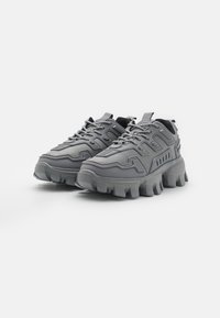Gray athletic shoes with a textured upper, thick sole, and prominent lacing system. Features molded accents and a chunky design.