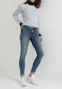 Šedý žebrovaný top s dlouhým rukávem v kombinaci se středně vybledlými skinny džíny a bílými teniskami. Džíny mají jemné vyblednutí a slim střih.