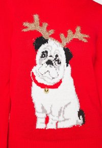 Pull rouge en tricot avec un carlin aux oreilles noires et au corps blanc, orné de bois de cerf dorés et d'un collier rouge avec une clochette.