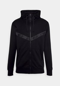 Svart zip-up hoodie i mjukt tyg med hög krage, framfickor och en tonad Nike-logoband över bröstet. Långa ärmar med upplagda muddar.