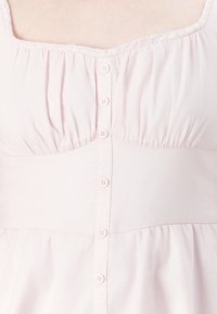 Top bottonato rosa chiaro con bordi in pizzo lungo lo scollo quadrato, caratterizzato da tessuto arricciato sopra il busto e dettaglio della cucitura in vita.