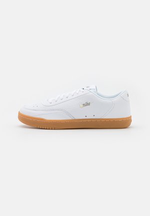 Hvit lær sneakers med teksturert overdel, rund tå og tan gummisåle; har gull logo og flate lissser.