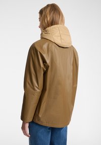 Giacca impermeabile marrone con cappuccio beige. Tessuto liscio, superficie leggermente lucida e vestibilità rilassata. Design semplice senza hardware visibile.