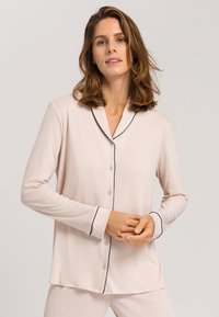 Lichtroze pyjamajack met lange mouwen, knoopsluiting aan de voorkant, contrasterende marineblauwe piping langs de kraag en manchetten, en een relaxte pasvorm.
