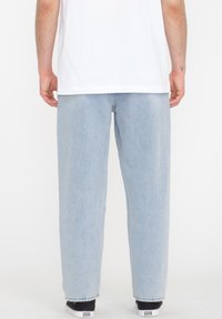 Light blue denim trousers with a relaxed fit, featuring a straight cut, visible stitching, and hemmed cuffs, paired with black sneakers.