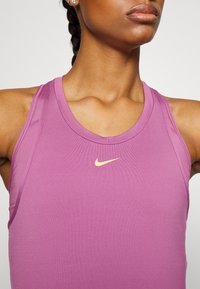 Paarse sporttanktop met een ronde hals en een gouden Nike-logo op de borst. Gemaakt van soepele, rekbare stof.