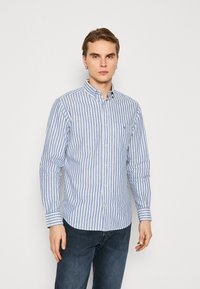 Camisa de botones a rayas en azul y blanco, de mangas largas, material de algodón suave, cuello y detalle sutil en el bolsillo del pecho.