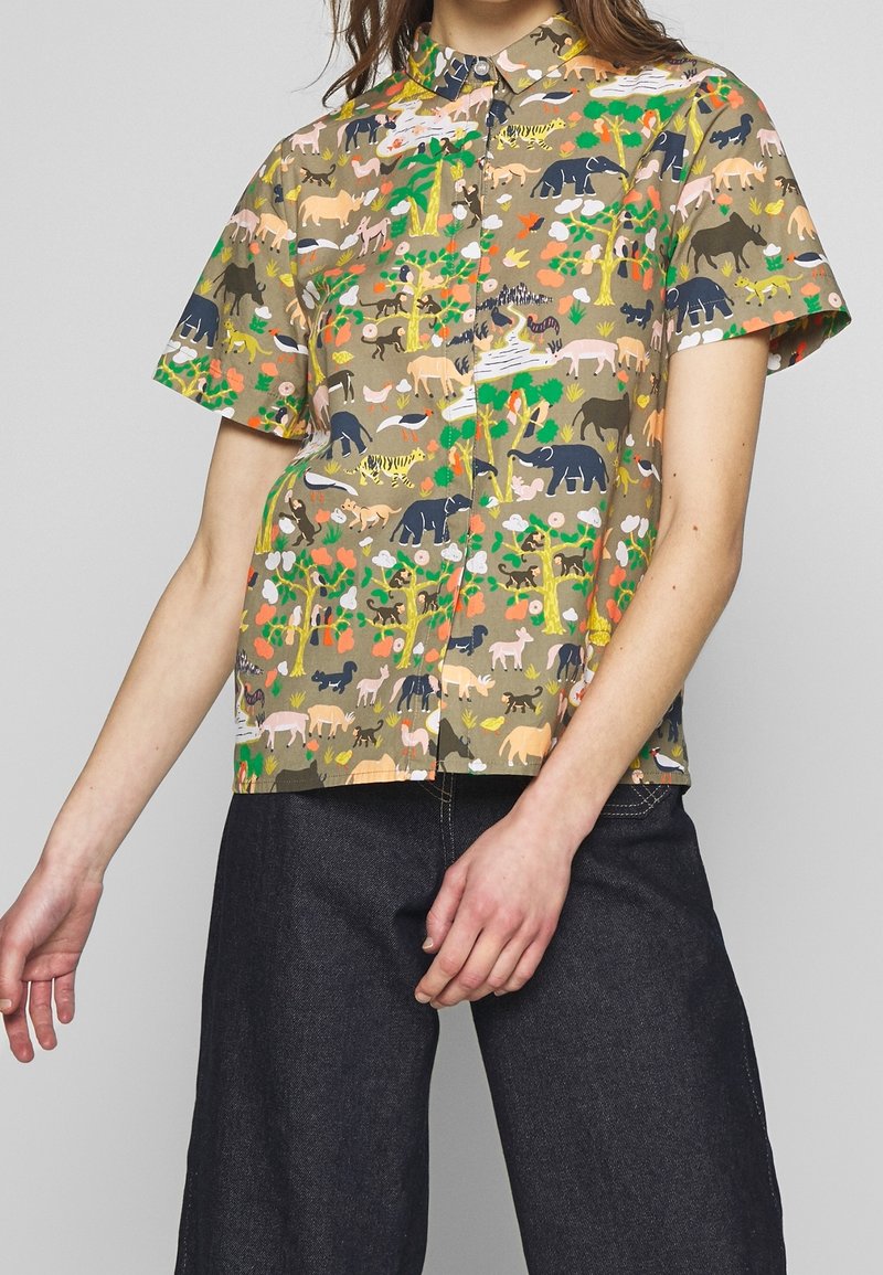 Košile s krátkým rukávem na knoflíky v vzorované tkanině s různými barevnými zvířaty a rostlinami na khaki pozadí.