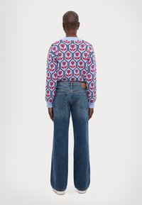 Suéter de punto con patrón floral en azul, rojo y rosa, combinado con jeans de mezclilla azul de pierna ancha. Vista trasera que muestra el diseño y el ajuste.