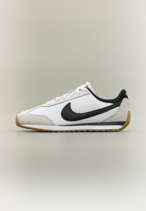 Baskets Nike blanches et beiges avec le logo noir, semelle gomme et lacets blancs, vues de côté sur un fond neutre.