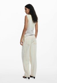 Top senza maniche di colore chiaro con un delicato motivo floreale, abbinato a pantaloni larghi crema con cuciture arancioni e lacci laterali.