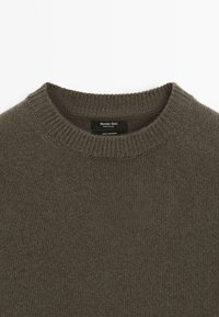 Tmavě olivově zelený kašmírový svetr s ribovaným kulatým výstřihem. Má hladkou texturu a štítek označující 100% kašmír.