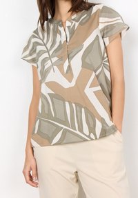 Maglietta a maniche corte in un tessuto leggero con un motivo astratto a foglia in tonalità di verde e beige, con scollatura a V.