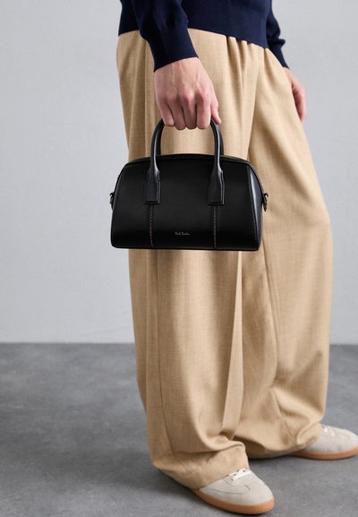 Schwarze Lederhandtasche mit strukturiertem Design, doppelten Griffen, subtilen Steppdetails und einem goldenen Logo. Kombiniert mit beigen weitgeschnittenen Hosen.