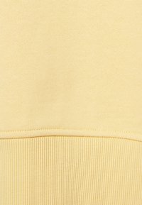 Tessuto di felpa giallo chiaro con una texture liscia e orlo a coste. Presenta un design semplice senza motivi o accenti visibili.