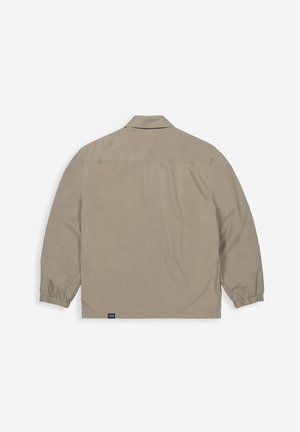 Light beige jacket with long sleeves, collar, elasticized cuffs, and a straight hem. Features a logo tag near the bottom left.