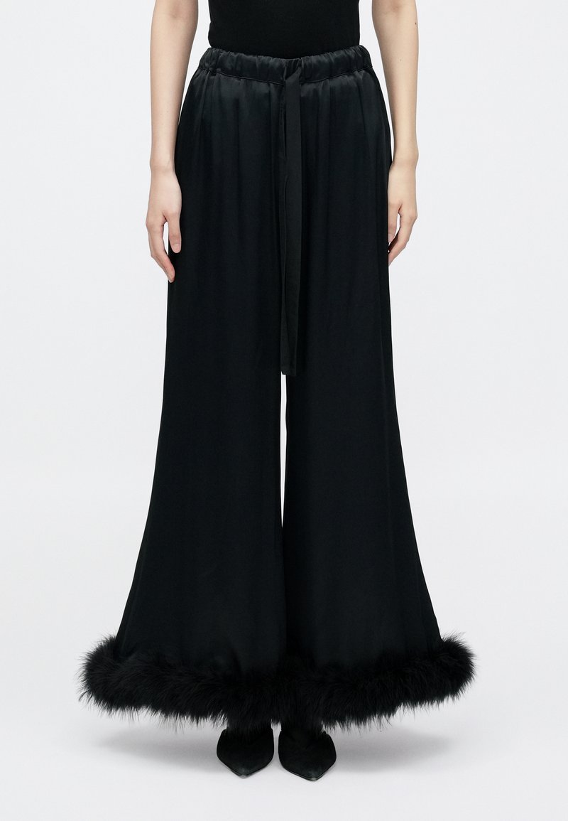 Crne široke hlače s satenskim završetkom; elastični pojas, odgovarajuća vrpca i umjetni krzneni rub na rubu. Nošene s crnim šiljastim cipelama.