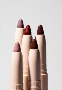Pięć beżowych sztyftów do ust w odcieniach różu, czerwieni i brązu, ułożonych na gładkim jasnym tle.