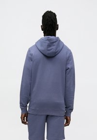 Kapucon pulover v enobarvni svetlo vijolični tkanini, z ohlapnim krojem, rebrastimi manšetami in robom ter detajlom kangguru žepa.