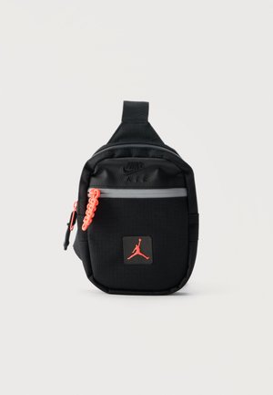 Μικρό μαύρο τσαντάκι Nike Air με μπροστινή τσέπη με φερμουάρ, πορτοκαλί τράβηγμα φερμουάρ και κόκκινο λογότυπο Jumpman σε λευκό φόντο.