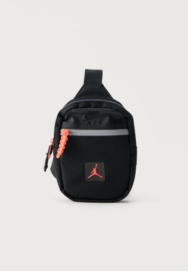 Μικρό μαύρο τσαντάκι Nike Air με μπροστινή τσέπη με φερμουάρ, πορτοκαλί τράβηγμα φερμουάρ και κόκκινο λογότυπο Jumpman σε λευκό φόντο.