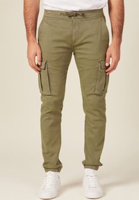 Olivgrüne Cargojogginghosen mit elastischen Bündchen, Kordelzugbund, Fronttaschen und zwei großen Seitentaschen. Der Stoff wirkt weich und langlebig.