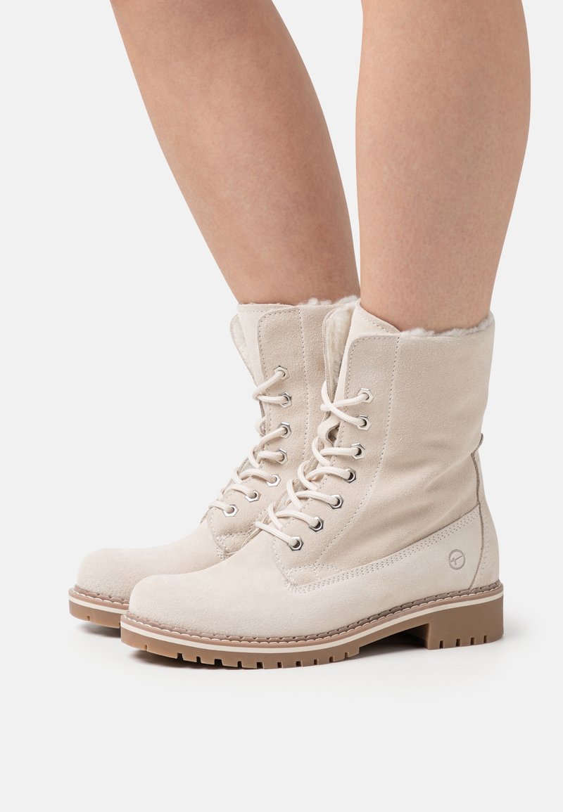 Botas de tobillo de ante beige con un suave forro de piel, que cuentan con ojales metálicos y cordones redondos, además de una suela de goma resistente para mayor tracción.