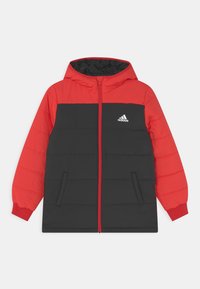 Veste matelassée rouge et noire avec capuche, fermeture éclair, poches latérales et un logo Adidas sur la poitrine gauche. Texture extérieure lisse.