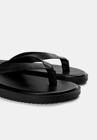 Infradito neri con cinturini larghi e piatti e una suola testurizzata. Realizzati in gomma liscia, presentano un design minimalista e senza branding visibile.