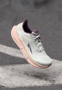 Chaussure de course avec un dessus gris clair, des accents violets et une semelle rose. Présente un design texturé et un système de laçage bien visible.
