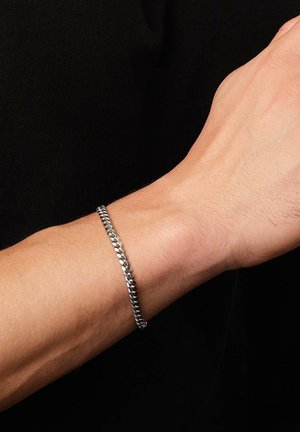 Braccialetto in argento con un design intrecciato e texture; indossato su un polso contro uno sfondo scuro, che mette in mostra una finitura lucida e elegante.