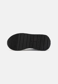 Suela de zapato de goma negra con agarre texturizado, que presenta estrías horizontales y verticales, y un logotipo en relieve. Bordes lisos y punta redondeada.