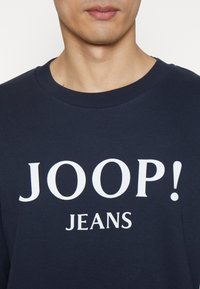 Felpa blu navy con grande scritta bianca "JOOP! JEANS." Realizzata in un tessuto morbido con design a girocollo classico.