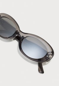 Grå, gjennomskinnelige solbriller med oval form og mørke, tonede glass. Har en glatt tekstur og subtile detaljer på rammen.