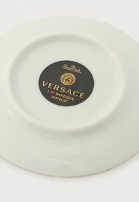 Parte inferior de un plato de porcelana blanca con etiqueta negra Versace Baroque Bianco y logo de Rosenthal en letras doradas.