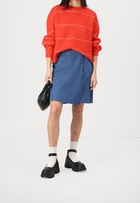 Punainen neulepaita, jossa on valkoiset raidat, farkku A-linjainen hame, musta käsilaukku ja paksut mustat nilkkurit valkoisilla sukilla.